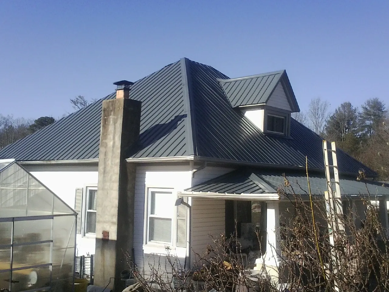 Dark blue standing seam metal roof on a white farmhouse with dormer — Slate & Tile Roof Repair by Roofing Brothers in Spurgeon