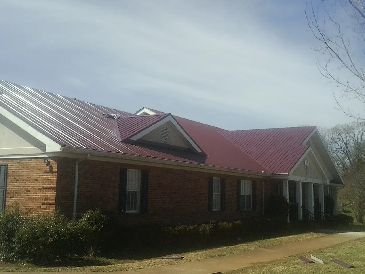 Red metal roof with gabled entries on a long brick building, from a Hail Damage Roof Repair job in Spurgeon