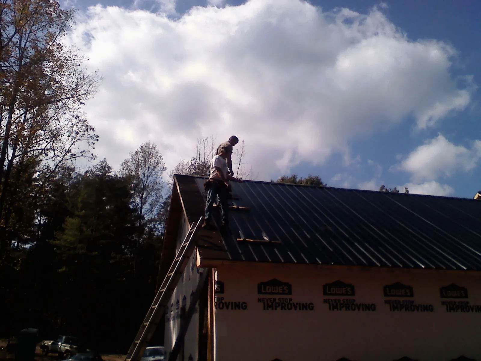 Roofer fastening dark metal panels high against a cloudy sky, from a Roof Inspection job in Spurgeon