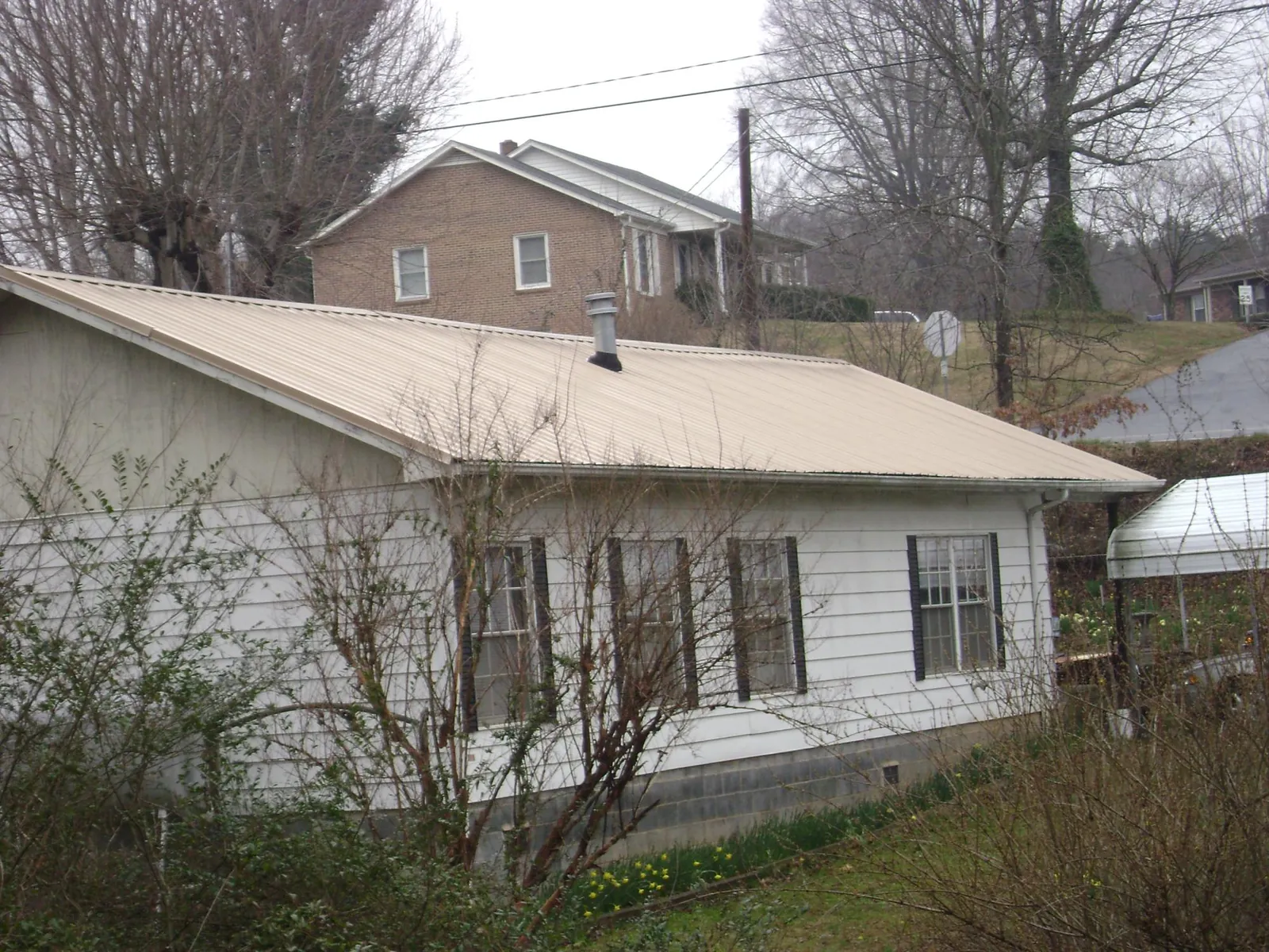 Tan metal roof on a white sided house set into a hillside — Commercial Roofing by Roofing Brothers in Spurgeon