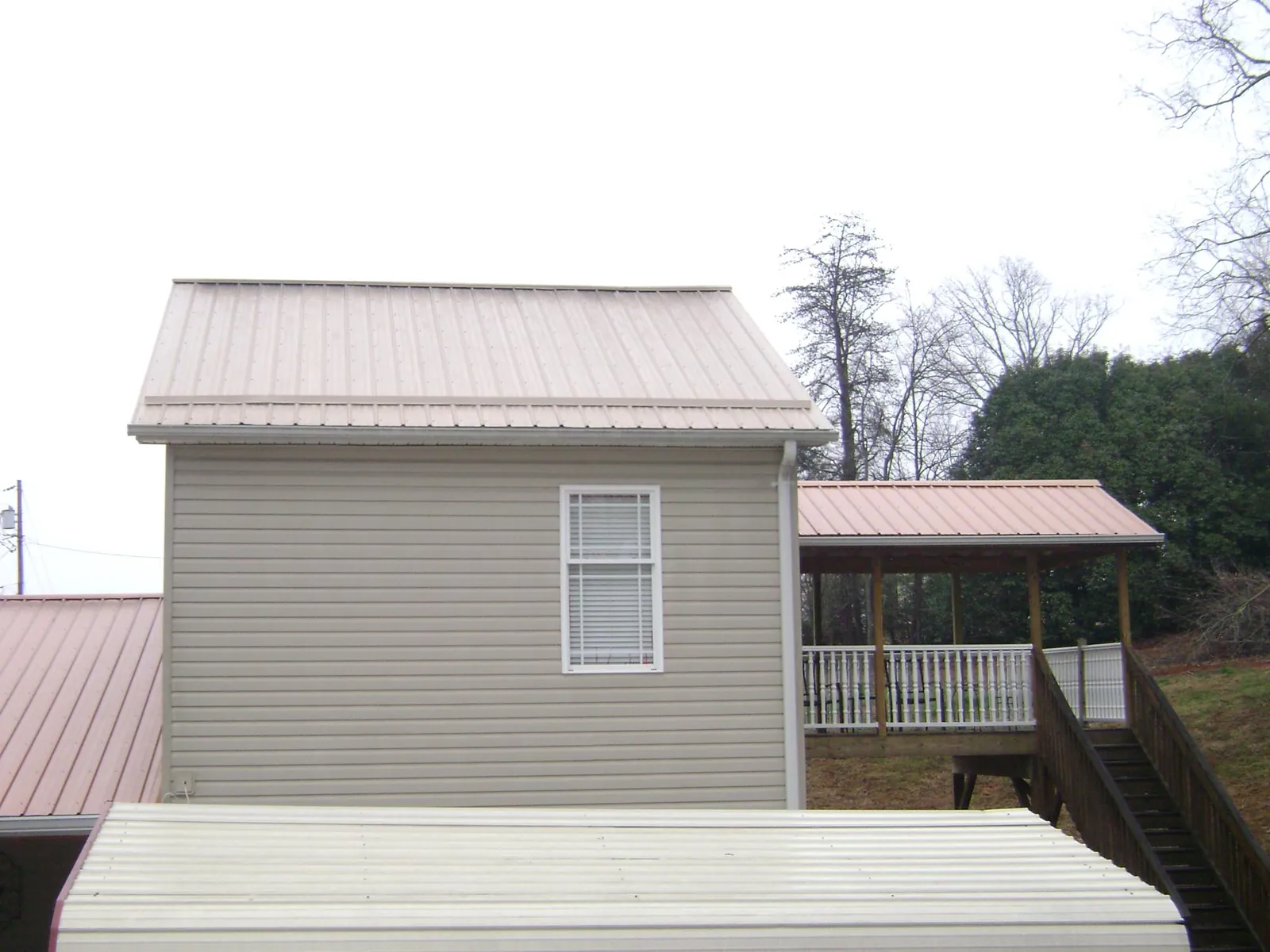 Tan metal roofs on a two story addition and attached porch, from a Roof Replacement job in Spurgeon